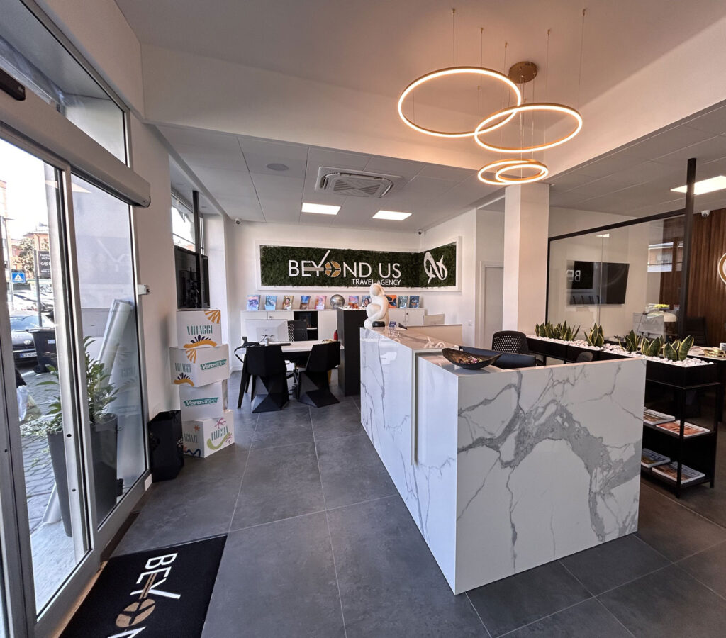 Agenzia viaggi Beyond Us con reception in marmo bianco, postazioni consulenti e design moderno personalizzato